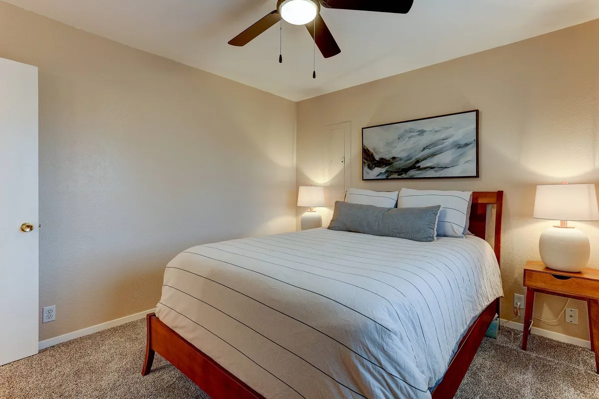 A tranquil bedroom scene showcasing a neatly made bed, elegant artwork, matching nightstands, and warm bedside lighting. The soft light and neutral tones evoke a sense of calm and privacy.