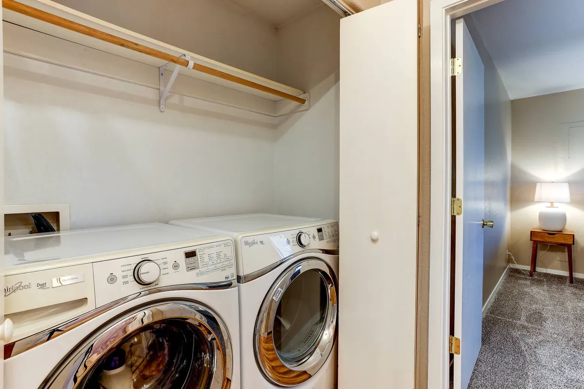 A practical in-house laundry space featuring a washer and dryer with a shelf above for organizing detergents and supplies. The area is well-lit and efficiently designed, offering everything needed for daily laundry needs.
