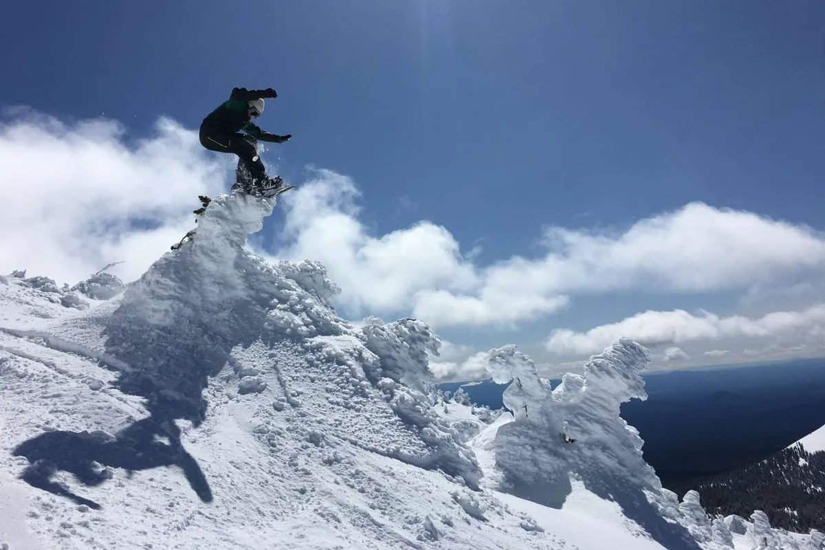 A snowboarder is mid-action against the backdrop of a snow-covered peak and dramatic clouds, capturing the exhilaration of winter sports in the mountains.