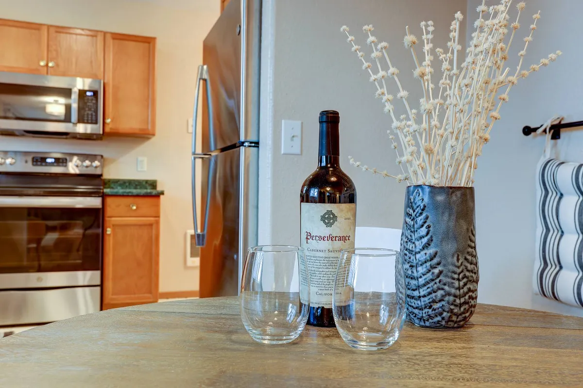 A welcoming kitchen scene with a bottle of wine, glasses, a vase with decorative branches, and visible kitchen appliances. The space feels ready for entertaining or casual dining, perfect for unwinding after a productive day.